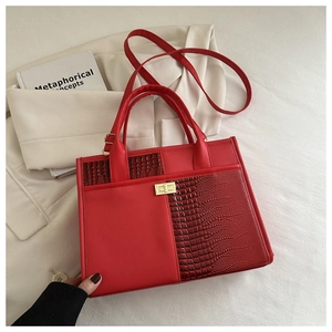 Detail view of red crocodile-pattern tote bag with golden twist lock on white fabric
