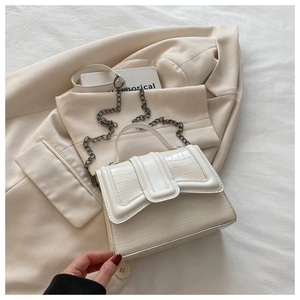 Detail der weißen Krokodil-Präge-Ledertasche mit dunkler Metallkette auf beigem Blazer