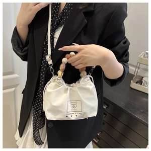 Close-up of a white pleated bucket bag with a colorful beaded handle and bear patch logo