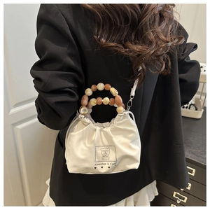 Chic white bucket bag with beaded handle and cute bear patch worn on a black blazer