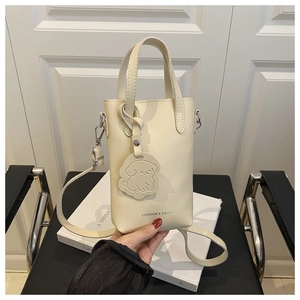 Détail d'un sac seau blanc crème avec un charm chien et une bandoulière amovible