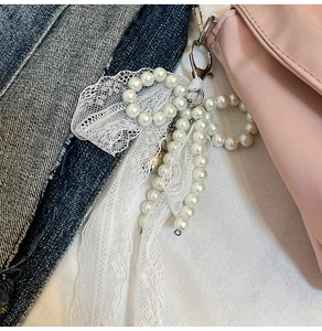 Detail of white pearl lace bow pendant with silver lobster clasp on a leather bag