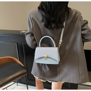 Chic light blue crossbody bag with textured flap and gold buckle styled on a grey blazer