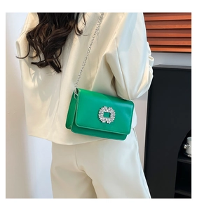 Detail of a bright green crossbody bag with a crystal square buckle and silver chain strap