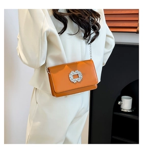 Detail of elegant orange crossbody bag with rhinestone buckle on white suit