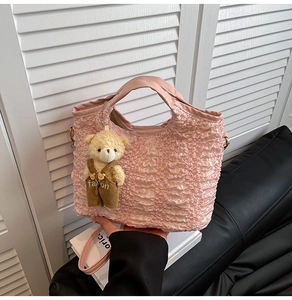 Detail of pink pleated tote bag with cute plush bear charm on white shutter background