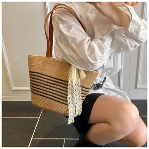 Close-up of straw woven tote with black stripes, leather handles and lace bow detail