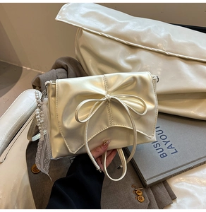 Détail d'un sac à main beige nacré avec un nœud délicat et un pendentif en perles