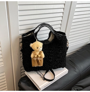 Détail d'un sac cabas noir gaufré avec un pendentif ours en peluche et bandoulière