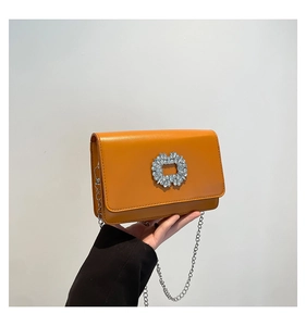 Detail of yellow leather crossbody bag featuring a sparkling rhinestone buckle and chain