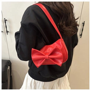 Close-up of a stylish red shoulder bag with a large bow detail worn by a model