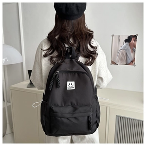 Detailed view of the black school backpack with a fashion smiley face logo on the front pocket