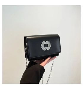 Close-up of black leather crossbody bag featuring a sparkling crystal floral buckle and chain