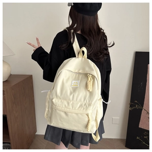 Détail d'un sac à dos jaune clair avec un écusson sourire et tirettes en corde tressée