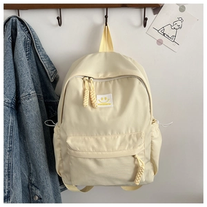 Détail du sac à dos en nylon crème avec écusson smiley et tirettes en corde tressée