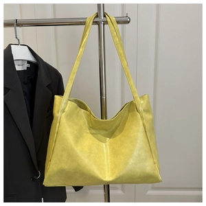 Détail d'un grand cabas en cuir jaune vif suspendu dans un décor de studio sobre