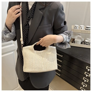 Detail of hand-woven cream straw tote bag with white handles and adjustable strap