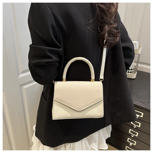 Detail of a beige crossbody bag featuring a textured V-weave flap and top handle