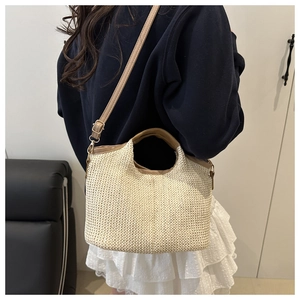 Detail of woven straw handbag featuring khaki leather handles and adjustable shoulder strap