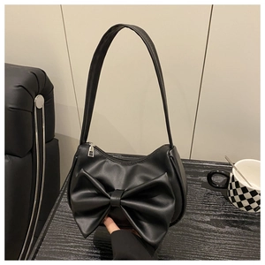Close-up of a black faux leather shoulder bag featuring a large decorative bow and silver zipper
