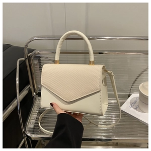 Detail view of woven texture on a cream crossbody flap bag with gold hardware
