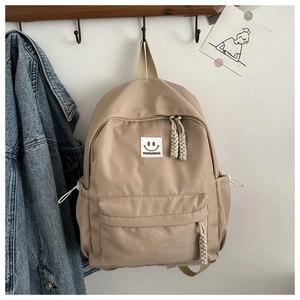 Détail du sac à dos beige avec écusson sourire, tirette tressée et poche latérale à cordon