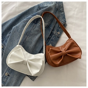 Close-up of white and brown crescent underarm bags with large bow detail on denim jacket