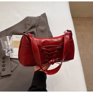 Détail du sac rouge verni avec lacets décoratifs croisés et fermeture éclair argentée