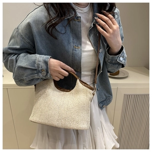 Detail of woven straw handbag with brown leather ring handles and adjustable strap