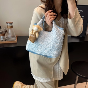 Sac bleu clair texturé avec pendentif ours en peluche présenté dans un décor doux