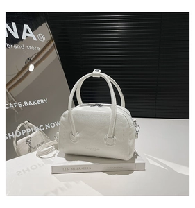 Close-up of white pebble leather Boston bag with silver zippers on a book