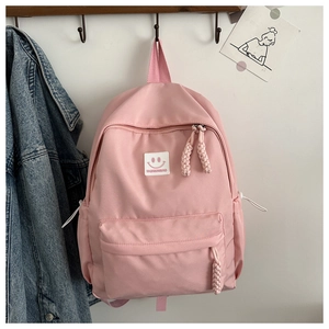 Détail d'un sac à dos rose avec écusson smiley et tirettes de fermeture en corde tressée