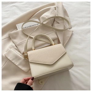 Macro detail of cream crossbody bag featuring woven V-pattern flap and gold hardware