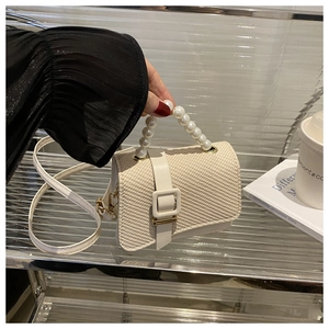 Close-up of cream woven handbag featuring decorative pearl handle and secure square buckle