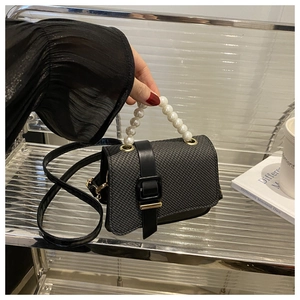 Close-up of black textured crossbody bag featuring elegant pearl handle and metal buckle