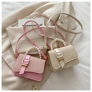 Detail of mini square bags featuring pearl handles and woven texture flap closure