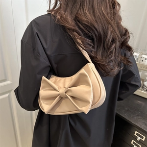 Elegant off-white shoulder bag with large bow detail shown on a model in a minimal room