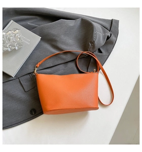 Orange lychee pattern bucket bag placed on a grey suit with golden hardware detail