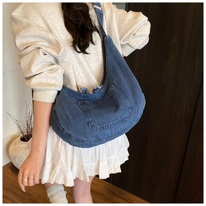Detail of blue denim hobo bag featuring a functional front pocket and rope zipper puller