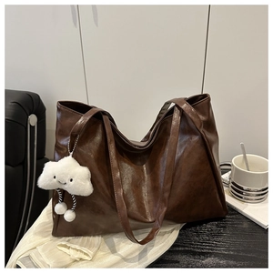 Detail einer dunkelbraunen Leder-Tote-Bag mit weißem Plüsch-Wolkenanhänger auf Sofa