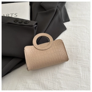 Detail of a beige crocodile-patterned handbag with a unique circular integrated handle
