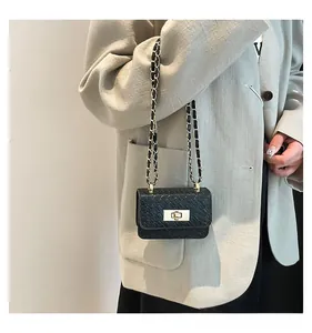 Detail of a black woven texture crossbody bag with gold chain strap and metal turn-lock