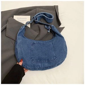 Macro detail of blue denim crossbody bag featuring frayed edges and functional front pocket