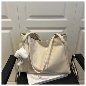 Detail of a large cream tote bag on a black chair with a white cloud plush pendant charm