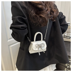 Vue détaillée du mini sac blanc avec nœud en diamant argenté sur un blazer noir