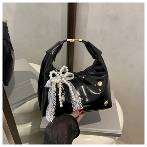 Close-up of black patent leather tote with a pearl lace bow and gold metal clasp