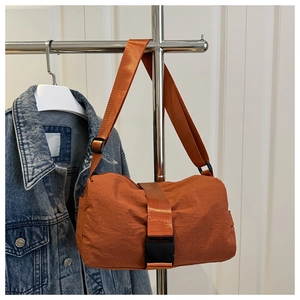 Detail of orange oxford fabric crossbody bag hanging on a hanger with wide shoulder strap