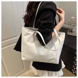 Close-up of a white tote bag with crocodile texture and slim shoulder straps