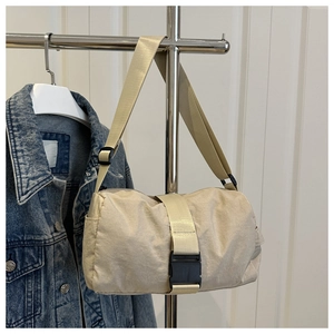 Detail of beige nylon cylinder crossbody bag with black plastic buckle and adjustable strap
