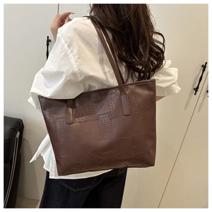 Detail of dark brown tote bag featuring embossed crocodile pattern and stitched leather panels